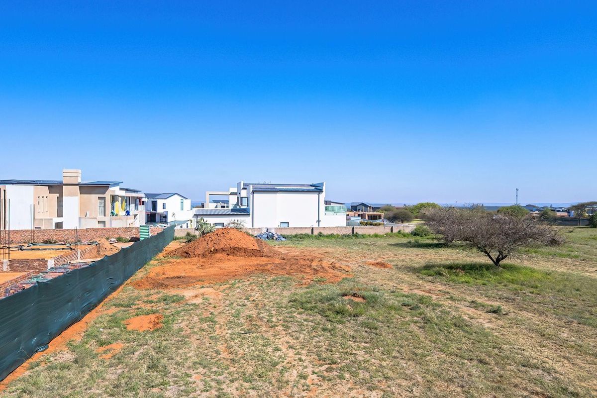 Aerial view of a vacant residential plot showing ongoing foundation work, boundary walls, and surrounding neighborhood development.
