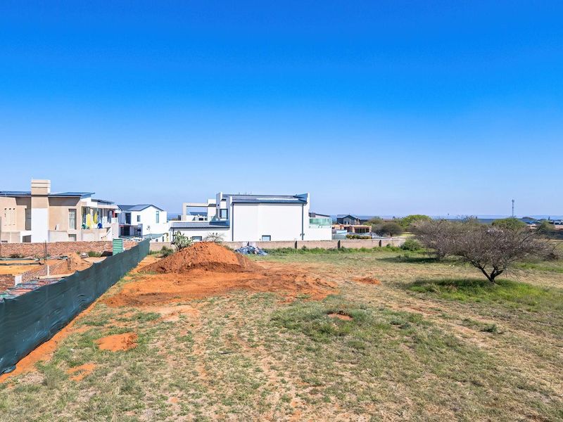 Aerial view of a vacant residential plot showing ongoing foundation work, boundary walls, and surrounding neighborhood development.