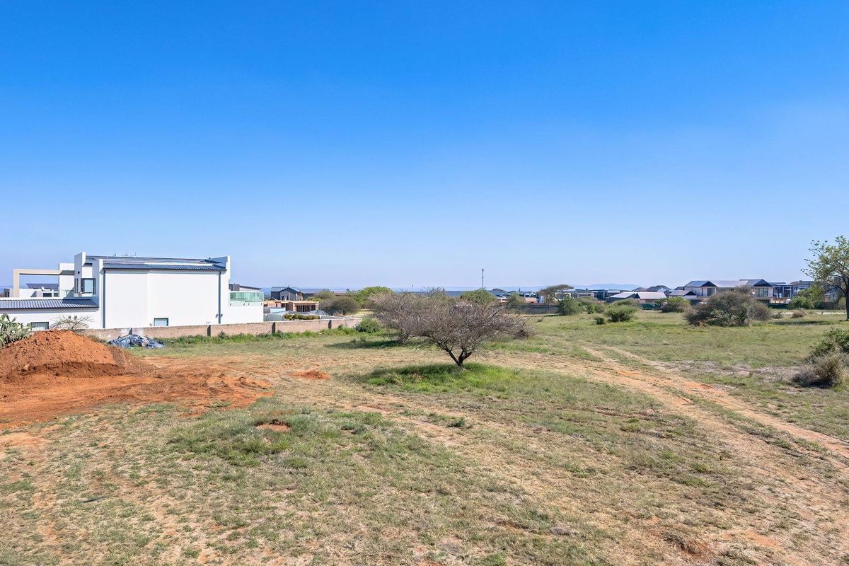 A vacant residential plot featuring natural vegetation, a boundary wall, and surrounding neighborhood views, suitable for new construction.