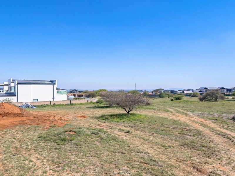 A vacant residential plot featuring natural vegetation, a boundary wall, and surrounding neighborhood views, suitable for new construction.