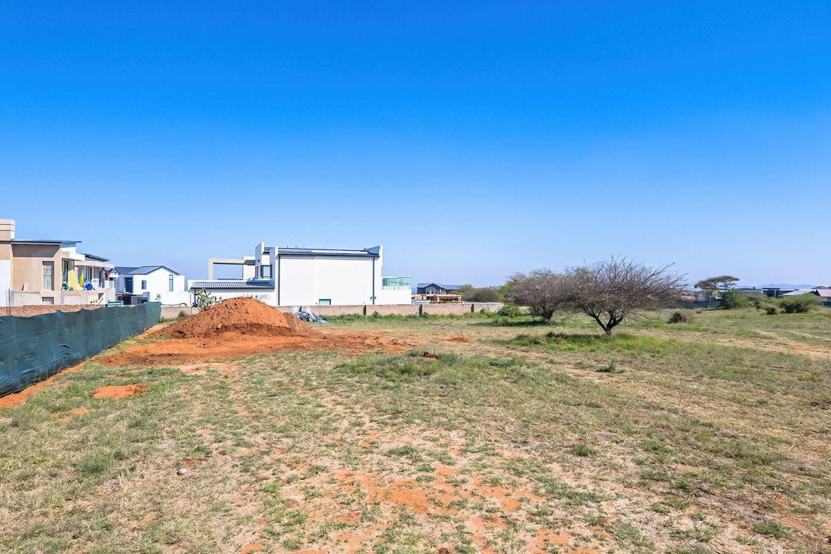 A vacant residential plot featuring natural grass, a soil mound, and perimeter fencing, situated in a developed neighborhood.