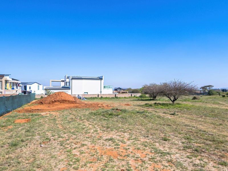 A vacant residential plot featuring natural grass, a soil mound, and perimeter fencing, situated in a developed neighborhood.