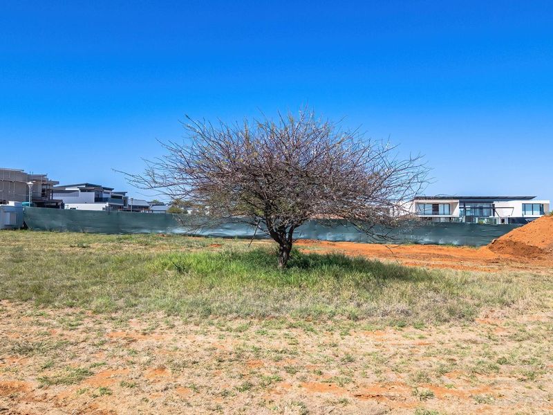 A view of a vacant residential plot featuring natural vegetation and perimeter fencing, situated within a developing residential estate.