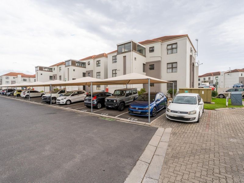 Exterior view of a multi-story apartment complex featuring covered parking bays and paved driveway access.