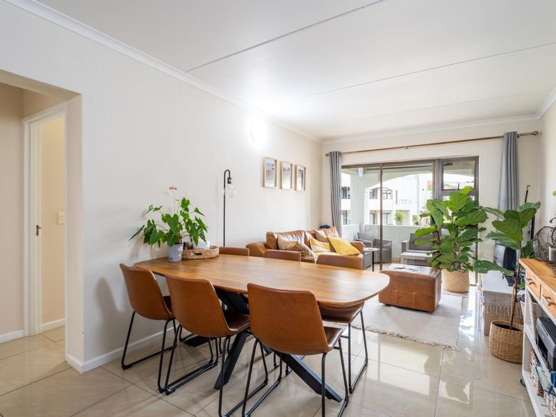 A bright open-plan living and dining area featuring tiled flooring and a large sliding glass door leading to an outdoor balcony.