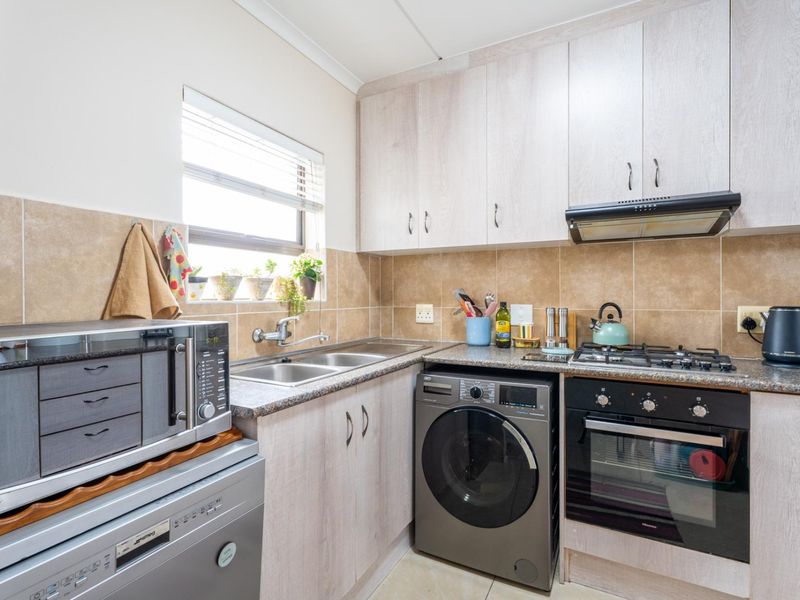 Compact kitchen featuring light wood-finish cabinetry, tiled backsplash, gas hob, built-in oven, extractor fan, and integrated laundry plumbing.
