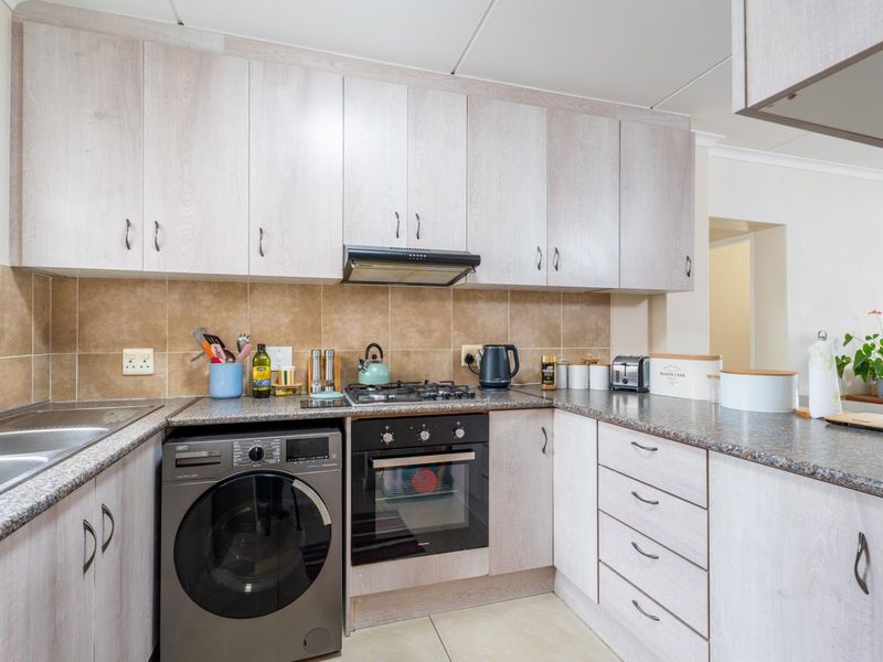 A functional kitchen featuring light wood-grain cabinetry, granite-look laminate countertops, a gas hob with extractor fan, and a built-in oven.