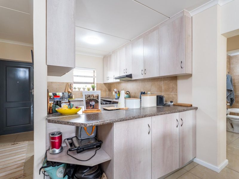 A functional kitchen featuring light-toned laminate cabinetry, durable countertops, a tiled backsplash, and an integrated extractor fan, with adjacent access to a bathroom.
