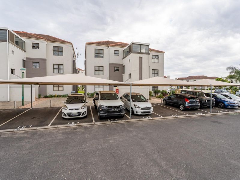 Exterior view of the apartment complex featuring designated covered parking bays with shade cloth structures and paved access.