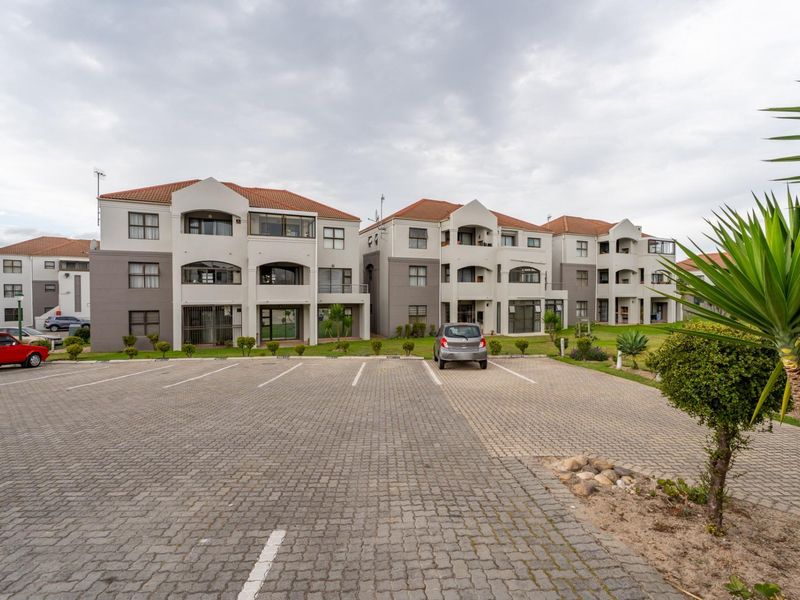 Exterior view of a multi-story apartment complex featuring a paved parking area and landscaped grounds.