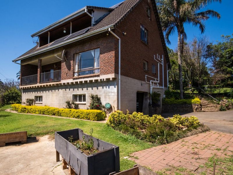 Rear view of a multi-story brick house featuring a balcony, solar panels, and a landscaped garden with paved pathways.