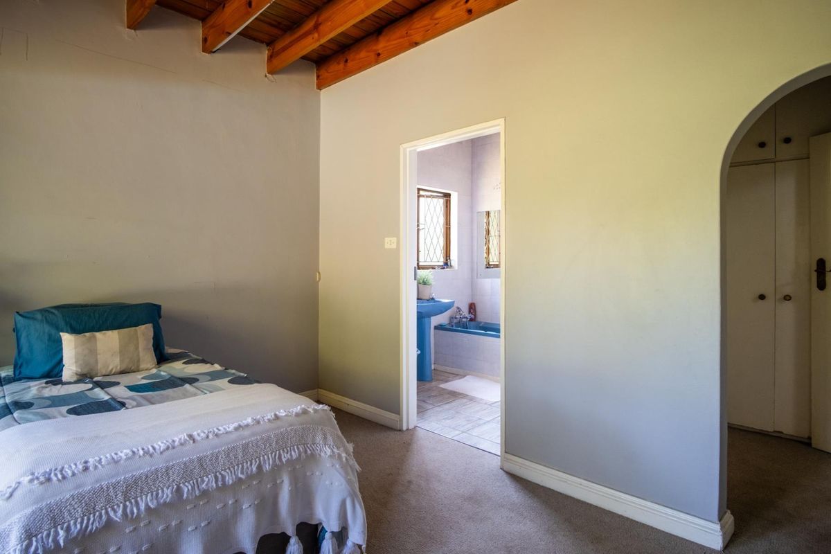 A bedroom featuring exposed timber ceiling beams, carpeted flooring, and an arched entryway leading to an en-suite bathroom with built-in storage.
