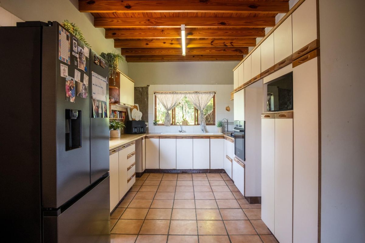 A functional kitchen featuring exposed timber ceiling beams, tiled flooring, ample built-in cabinetry, and a double sink with a window view.