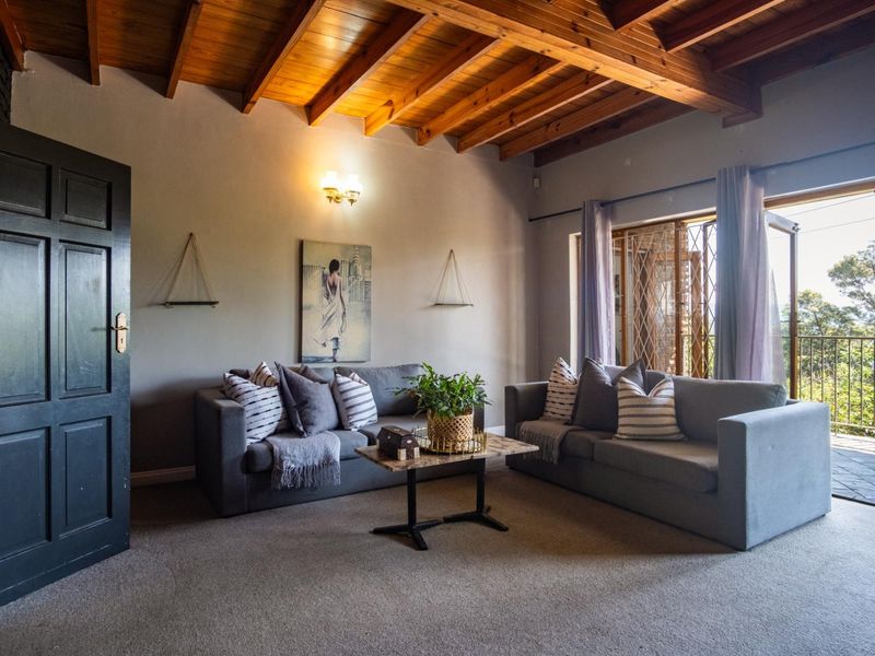 A cozy living room featuring an exposed timber beam ceiling, neutral walls, and sliding glass doors that open to an outdoor balcony area.