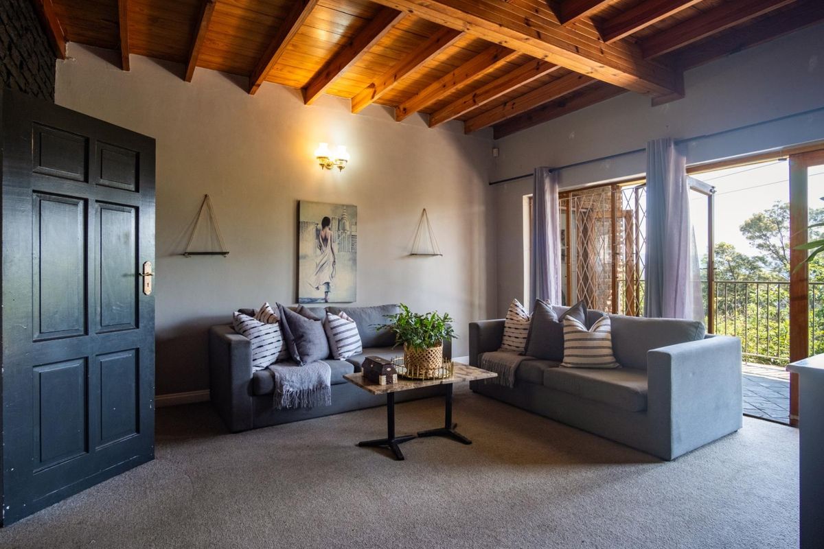 A cozy living room featuring an exposed timber beam ceiling, neutral walls, and sliding glass doors that open to an outdoor balcony area.