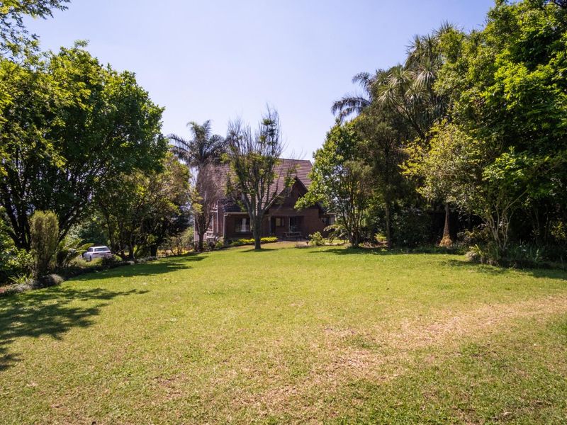 A spacious rear garden featuring a large lawn and mature trees, providing a private setting for the brick-faced house with a tiled roof.