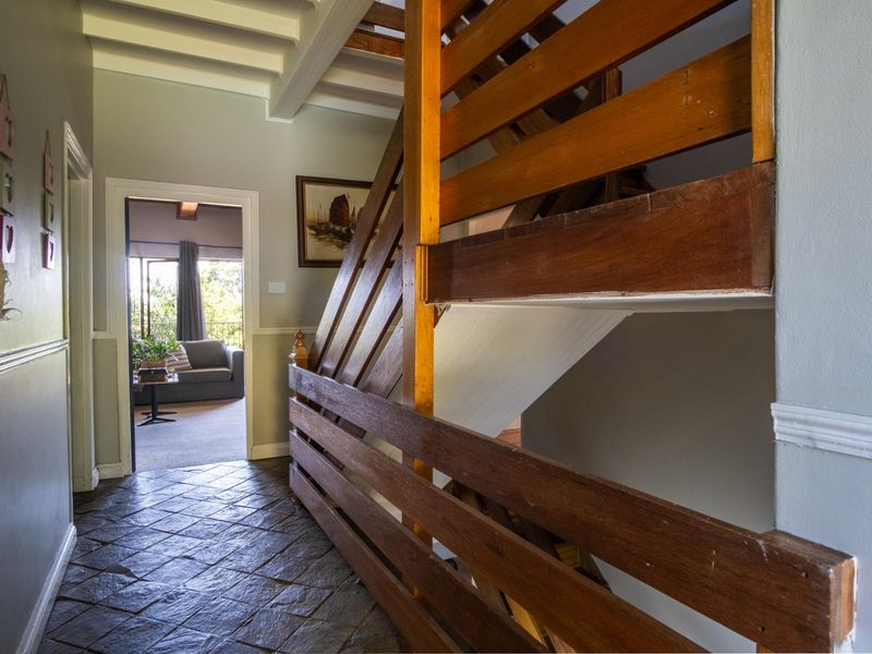 A characterful hallway featuring rustic stone tile flooring, exposed ceiling beams, and a prominent timber staircase with a traditional wooden balustrade.