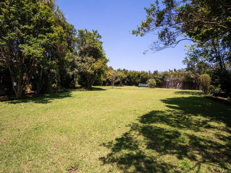 A spacious, well-maintained private garden featuring a large lawn area surrounded by mature trees and perimeter fencing.