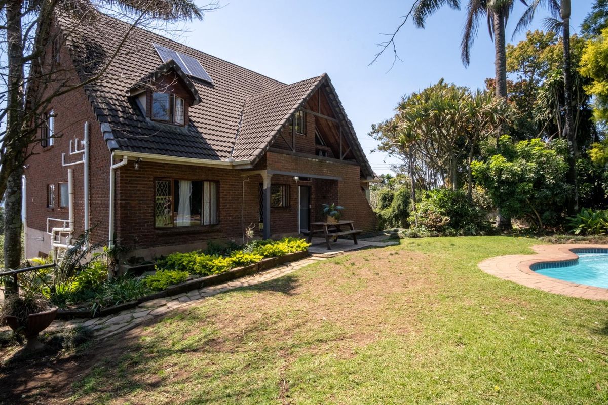 Rear view of a double-story brick house featuring a tiled roof with solar panels, dormer windows, and a swimming pool set in a garden.