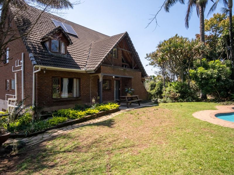 Rear view of a double-story brick house featuring a tiled roof with solar panels, dormer windows, and a swimming pool set in a garden.