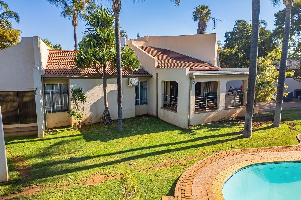 Rear view of the property featuring a swimming pool with brick coping, a covered patio area, and established garden surroundings.