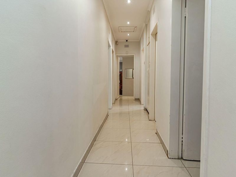 A clean and well-lit hallway featuring neutral tiled flooring and recessed ceiling lighting, providing access to multiple rooms within the property.
