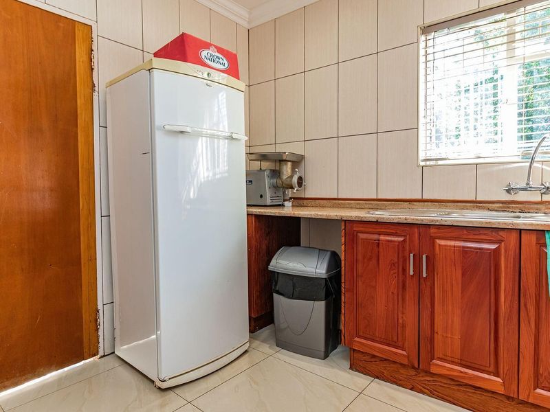 A functional scullery area featuring tiled walls, built-in wooden cabinetry with stone countertops, and a stainless steel sink.