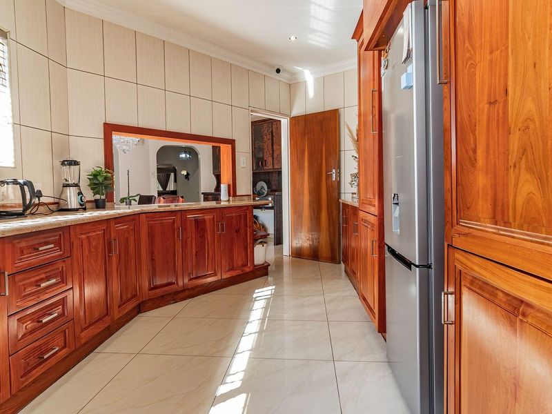 A well-maintained kitchen featuring warm wooden cabinetry, stone countertops, tiled splashbacks, and large format floor tiles with ample storage space.