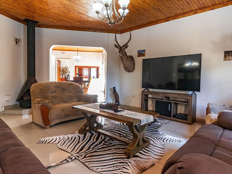 Spacious living room featuring a wood-paneled ceiling, tiled flooring, and a cozy freestanding fireplace, with an open-plan flow to the adjacent dining area.