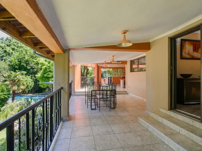 A spacious covered patio featuring tiled flooring, wrought iron railings, and direct access to the interior through sliding glass doors, overlooking the garden area.