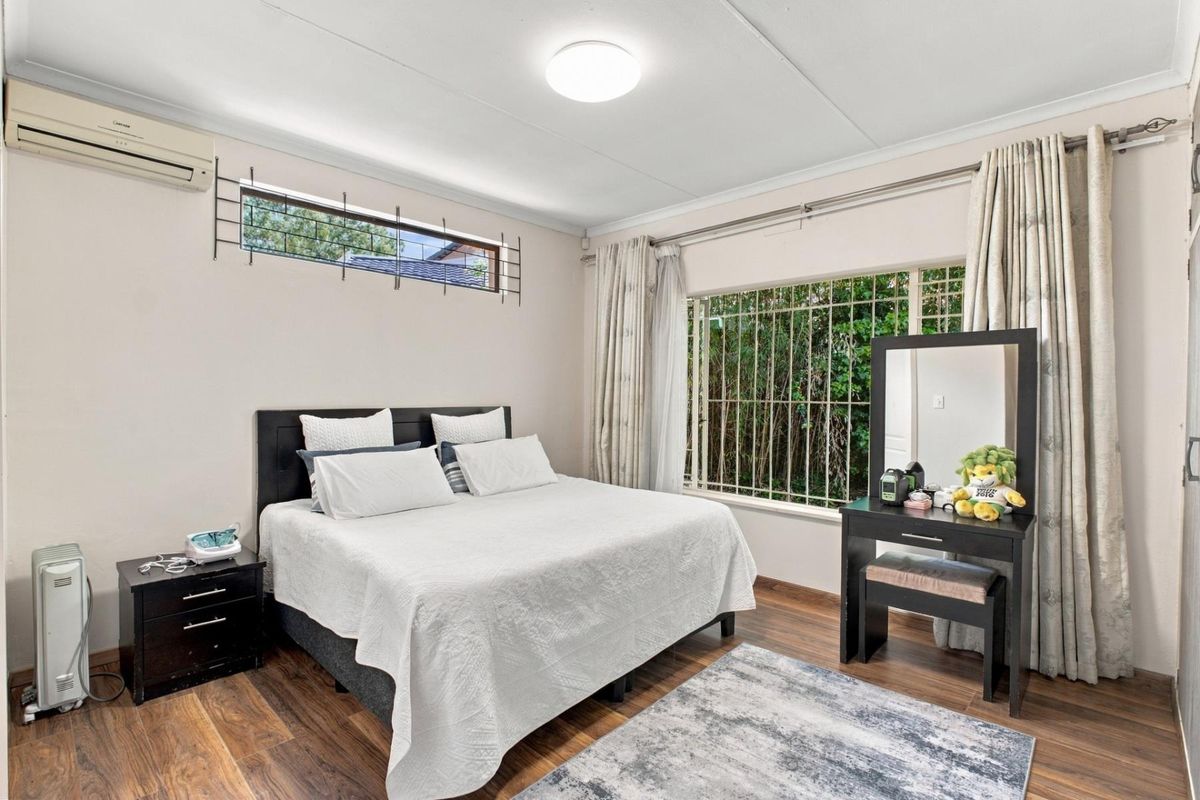 A well-maintained bedroom featuring laminate flooring, a split-system air conditioner, and security bars on the windows for added peace of mind.