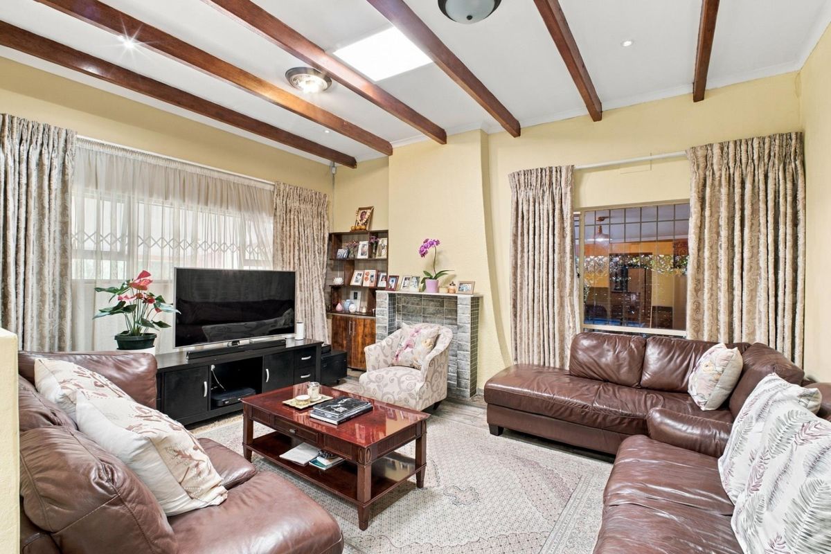 Spacious living room featuring exposed timber ceiling beams, a central skylight, and a built-in fireplace, offering a warm and inviting atmosphere.