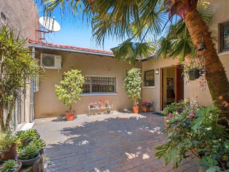 A private rear courtyard featuring brick paving, established landscaping, and an exterior wall-mounted air conditioning unit.