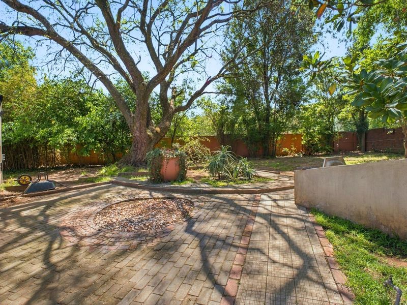 A spacious garden area featuring mature trees, brick-paved pathways, and a perimeter wall, offering a private outdoor space with established landscaping.