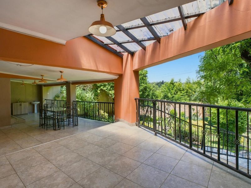 Spacious covered patio featuring tiled flooring, wrought iron railings, and a built-in sink area, overlooking a lush garden setting.