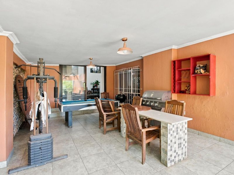 Covered patio area featuring a built-in braai, stone-clad breakfast bar, and tiled flooring, suitable for outdoor entertaining.