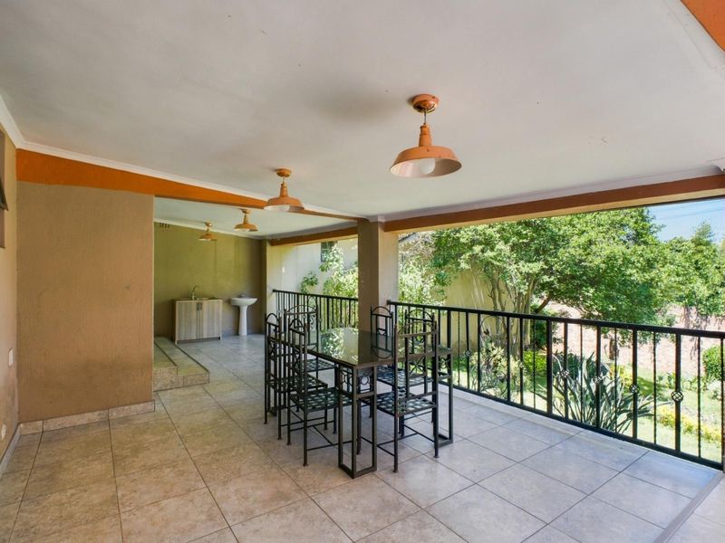 A covered outdoor patio featuring tiled flooring, a metal balustrade, and a built-in sink area, overlooking the garden.