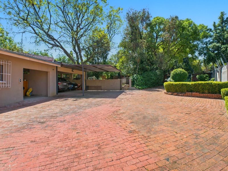 Spacious front exterior featuring a large brick-paved driveway, a covered carport, and established garden landscaping with secure boundary walls.