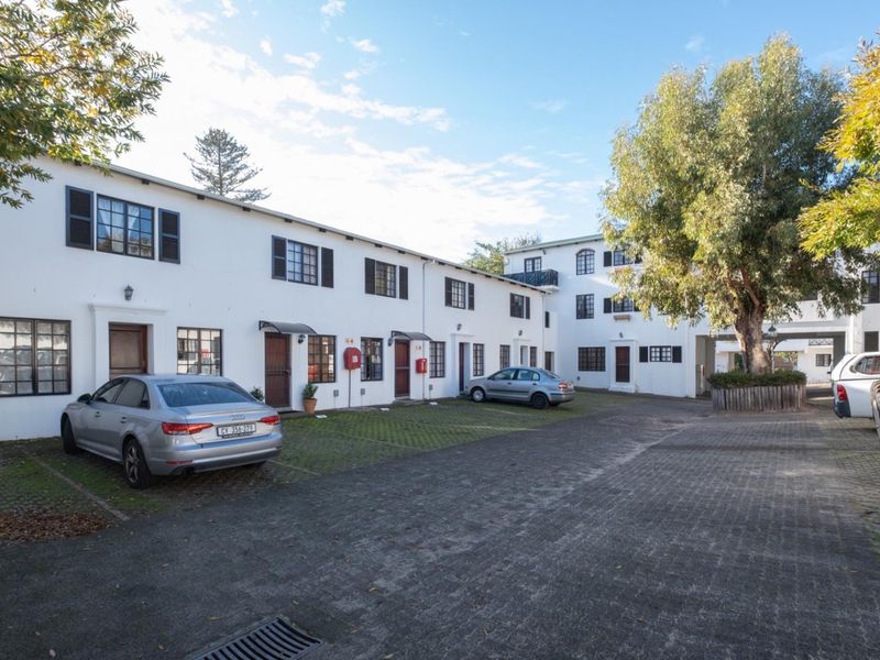 Exterior view of a multi-unit apartment complex featuring a paved parking area, white facade, and secure access points.