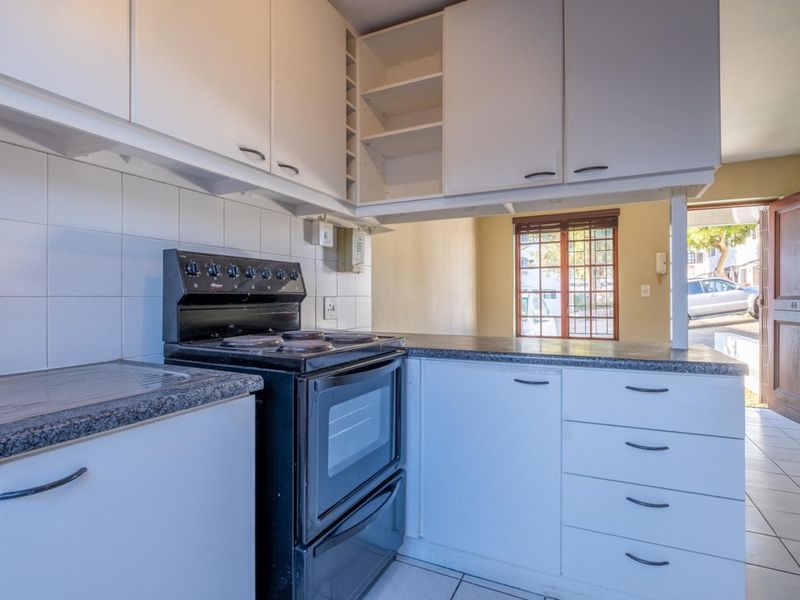 A functional kitchen featuring white cabinetry, laminate countertops, a freestanding electric stove, and tiled flooring, with direct access to the exterior.