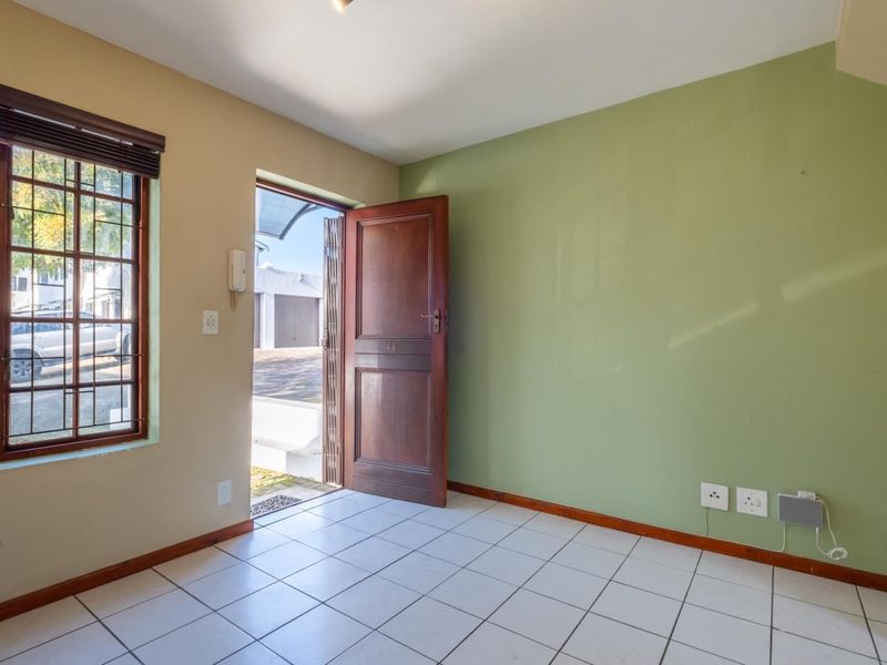 An empty entrance area featuring tiled flooring, a timber door with a security gate, and an intercom system, providing direct access to the exterior.