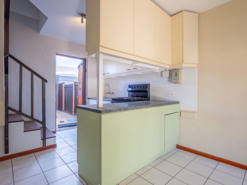 A compact kitchen featuring built-in cabinetry, a tiled backsplash, and a freestanding stove, with direct access to an outdoor area via a side door.