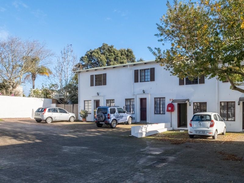 Front exterior view of the apartment complex featuring a paved parking area, white facade, and security features.