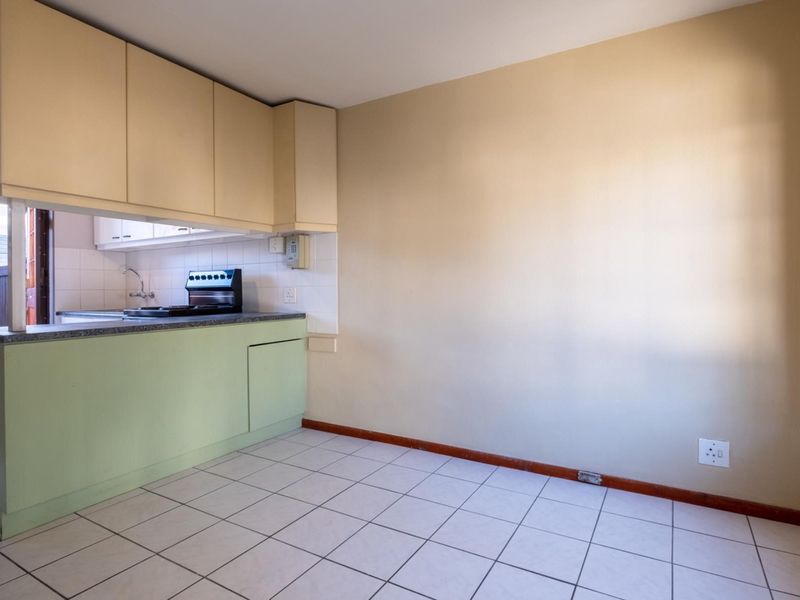 A compact, empty kitchen area featuring tiled flooring, built-in cabinetry, and a functional counter space, offering a blank canvas for potential renovation.