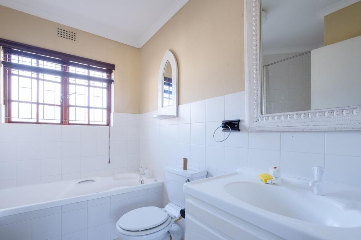 A functional bathroom featuring a built-in bathtub, vanity basin, toilet, and tiled walls, with a window providing natural light.