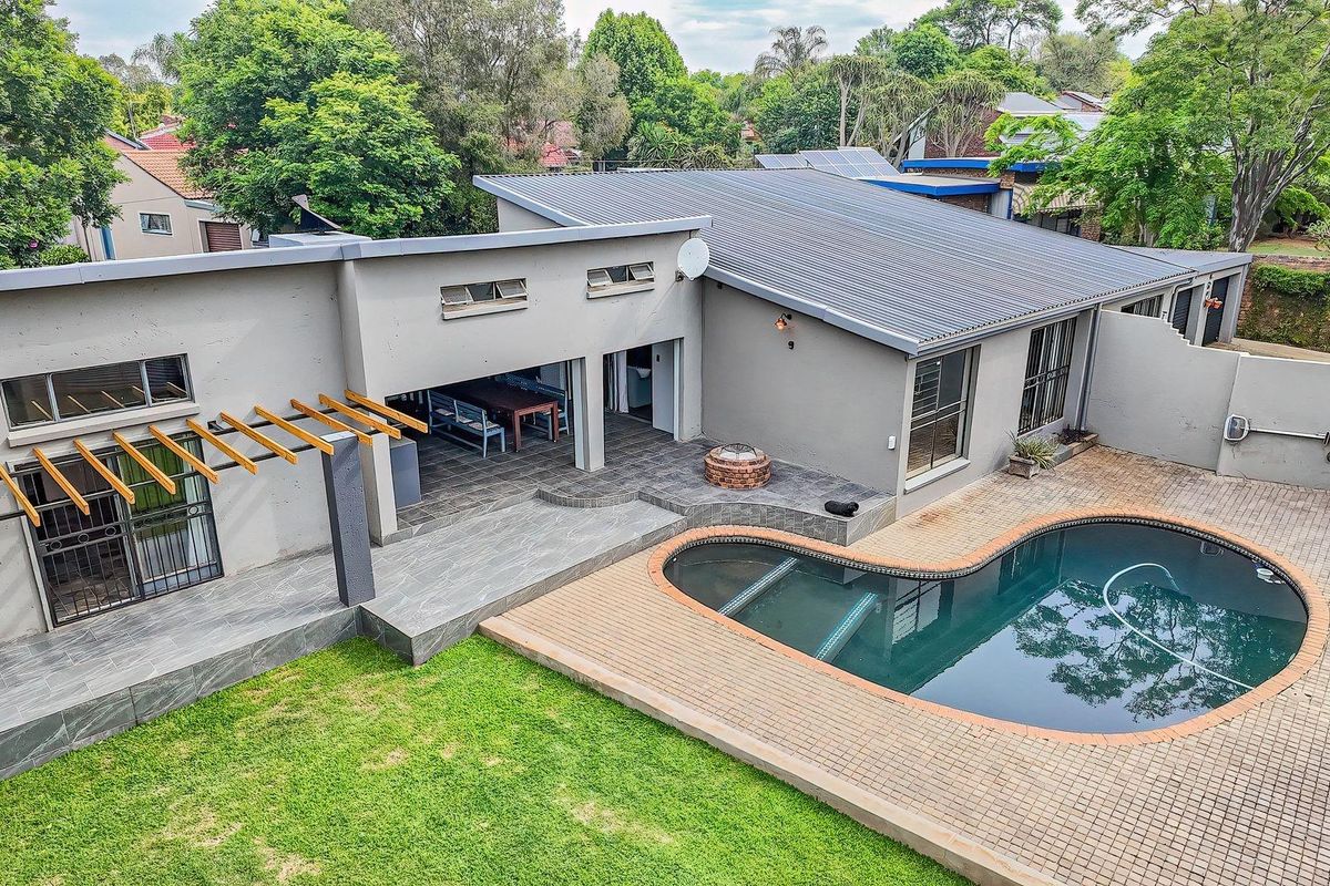 Aerial view of the rear garden featuring a swimming pool, paved pool deck, covered patio with timber pergola, and well-maintained lawn.