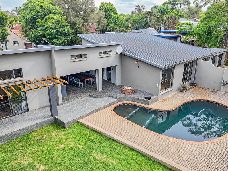 Aerial view of the rear garden featuring a swimming pool, paved pool deck, covered patio with timber pergola, and well-maintained lawn.