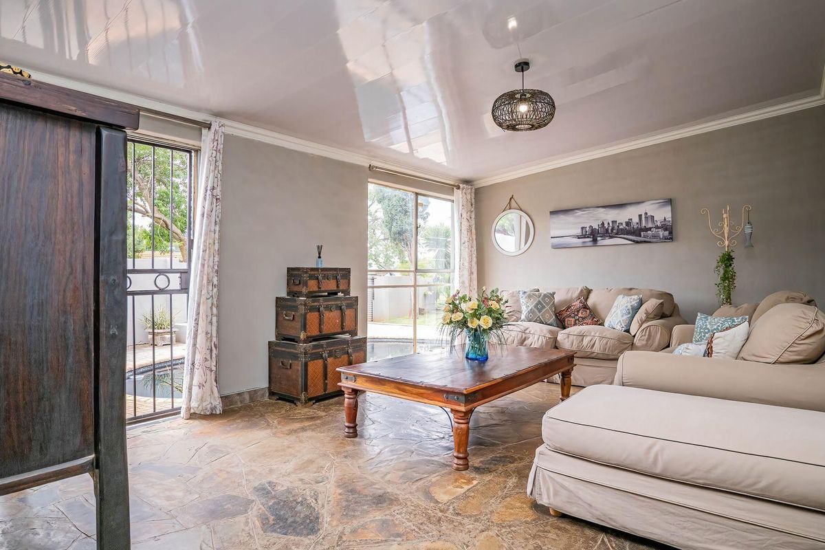 Spacious living room featuring natural stone flooring, a high-gloss ceiling, and direct access to the outdoor pool area through sliding glass doors.