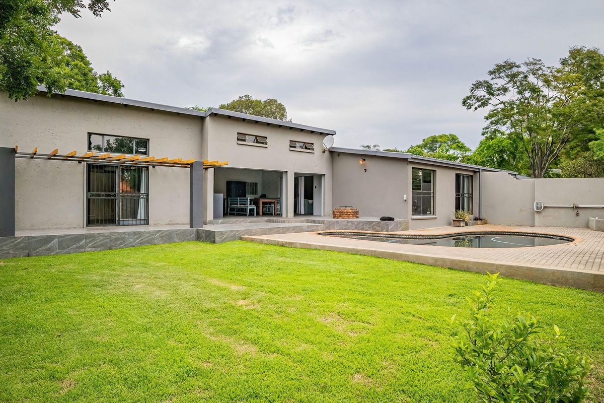 Rear view of the property featuring a spacious lawn, swimming pool with paved surround, and a covered patio area with a timber pergola.