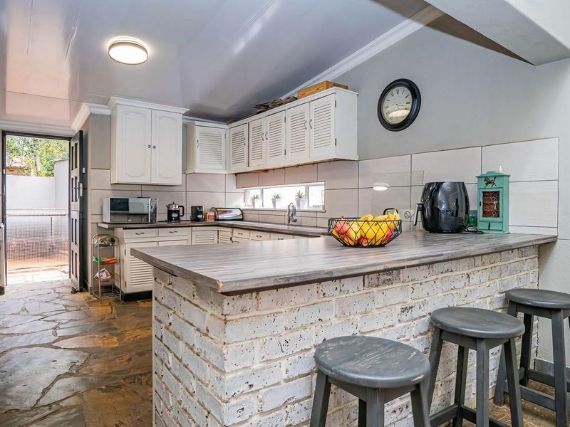 A functional kitchen featuring white cabinetry, a rustic brick breakfast bar, stone flooring, and a tiled backsplash with direct access to an outdoor area.